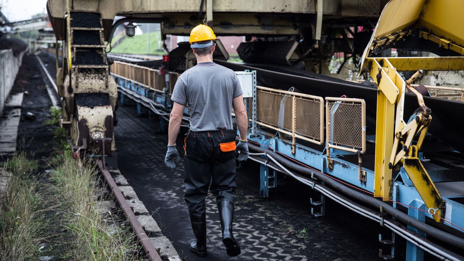 Trabalhador de costas caminhando ao lado de máquinas em uma planta industrial