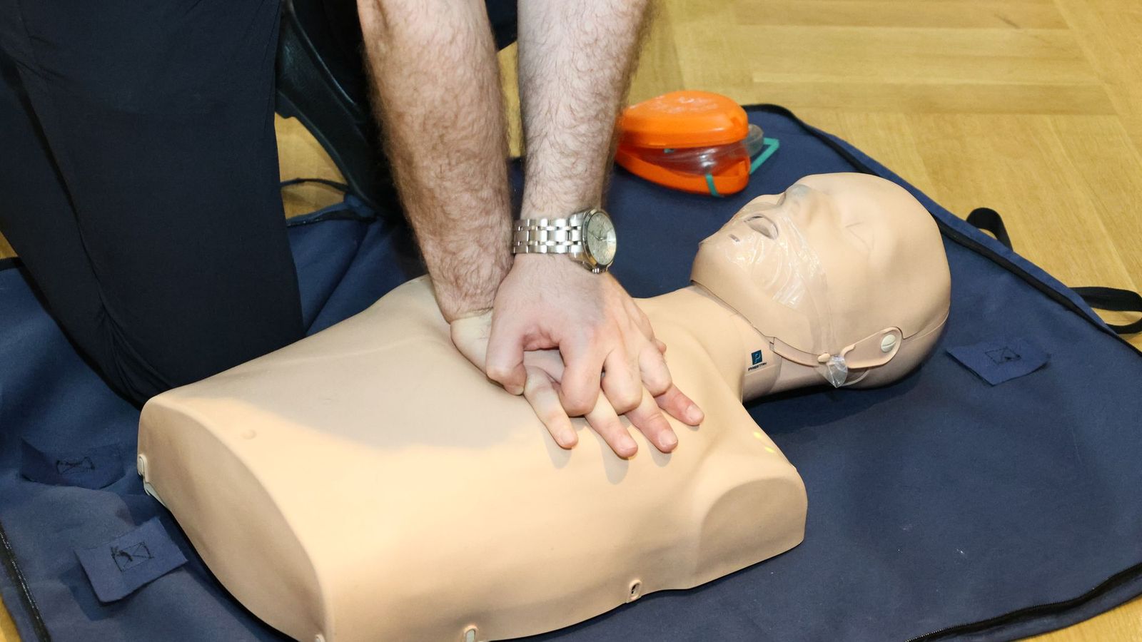 Mãos praticando massagem cardíaca em manequim durante treinamento de primeiros socorros
